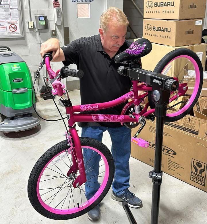 A volunteer assembling a pink child’s bicycle on a repair stand