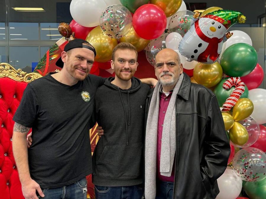 Three men standing together in front of a Christmas balloon arch