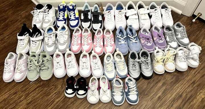 Twenty-four pairs of new children’s Nike and Jordan sneakers arranged in rows on a wood floor