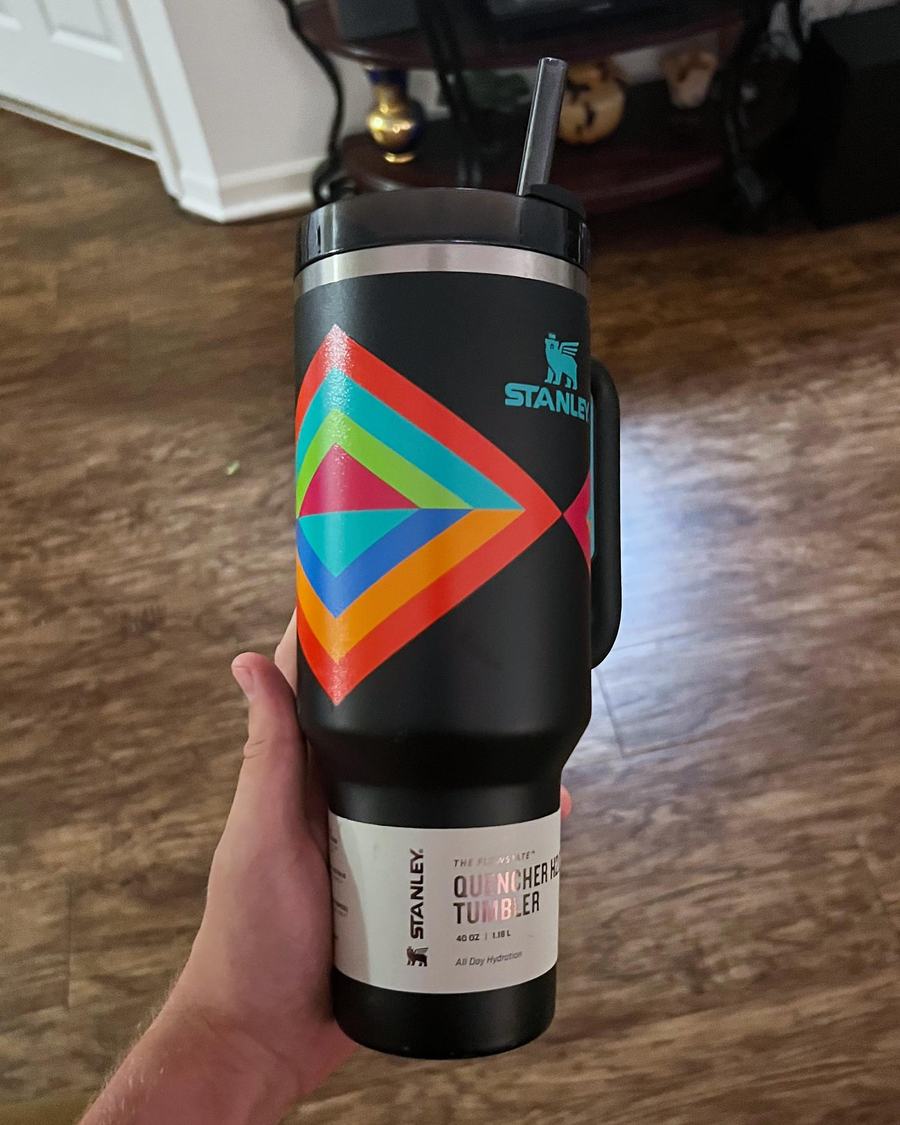 A hand holding one new black Stanley Quencher tumbler with a multicolored diamond design and its white 40 oz Quencher label facing the camera
